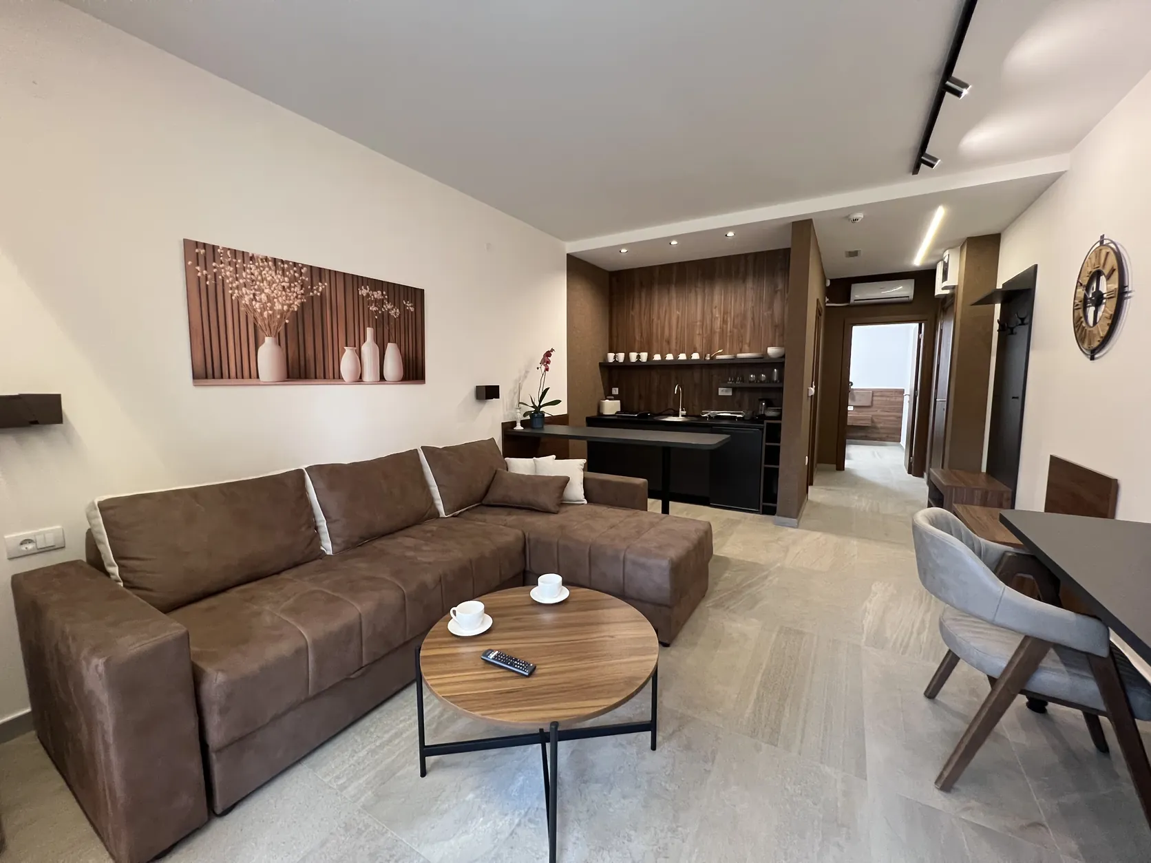 Dnevna zona apartmana – ugaona garnitura, kuhinja sa zidnom oblogom od drveta i trpezarijski sto