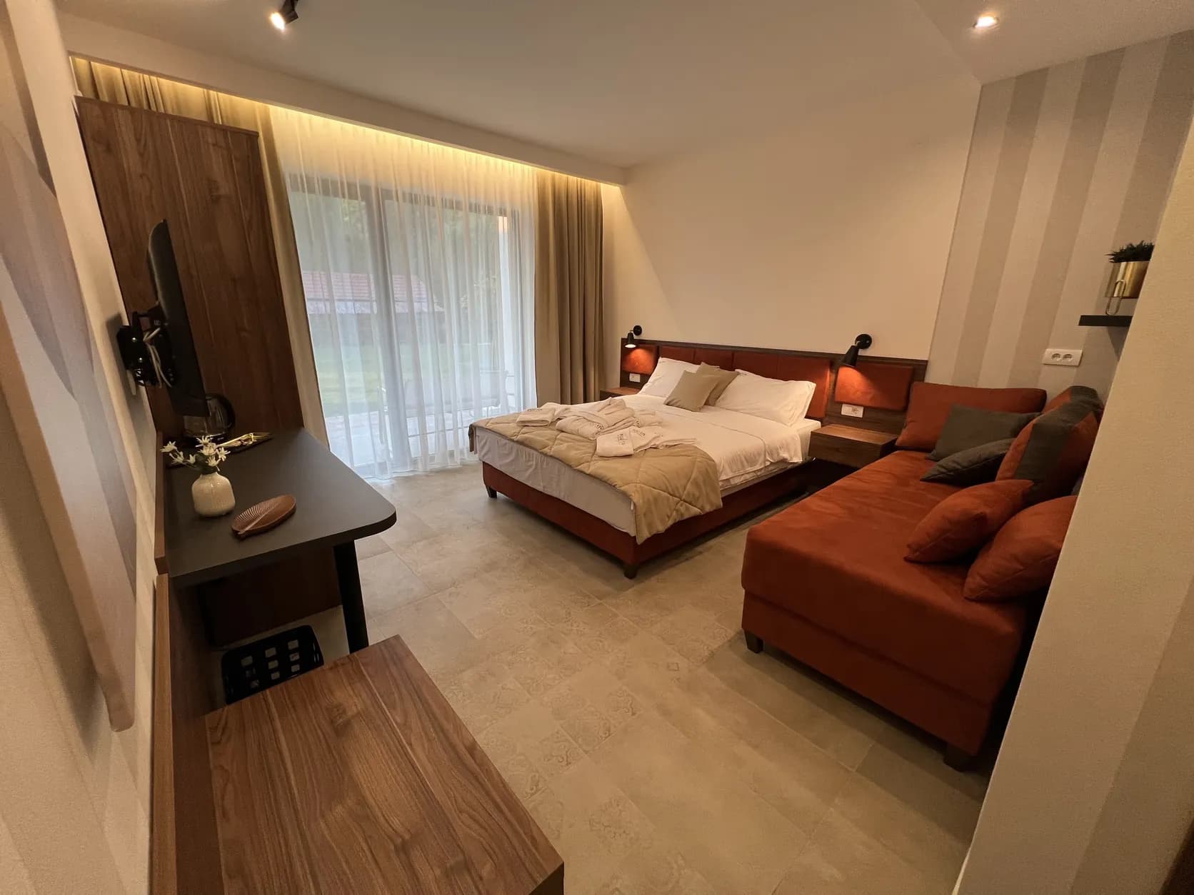Studio sa francuskim ležajem, sofom i indirektnom rasvetom u spuštenom plafonu, uz staklena vrata ka dvorištu