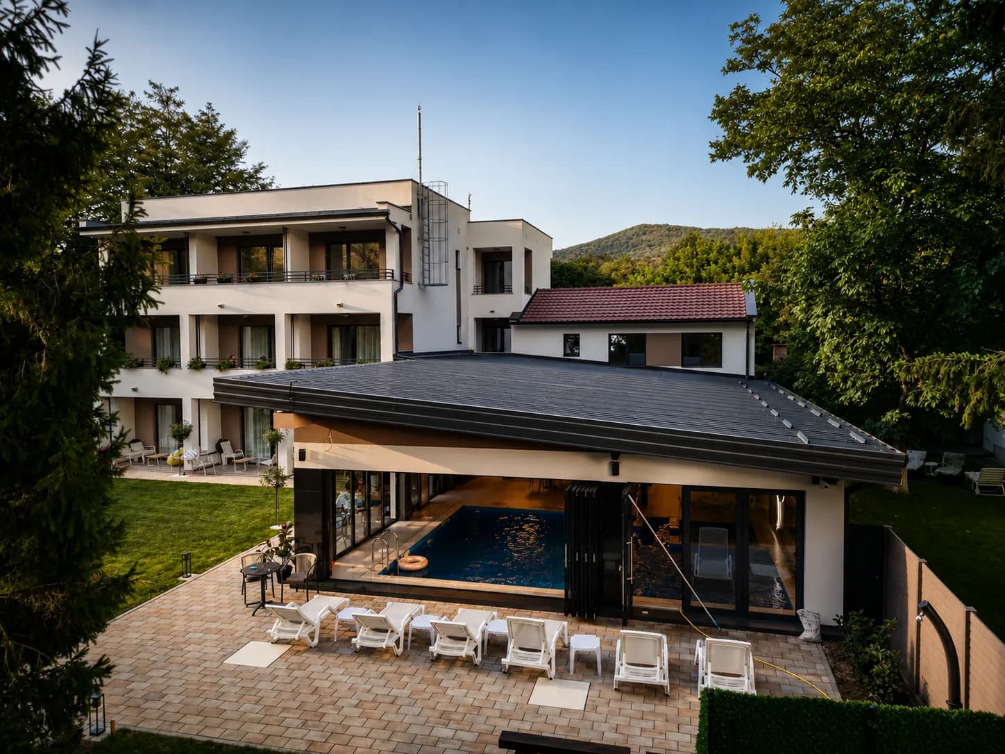 Pogled odozgo – objekat zatvorenog bazena sa otvorenim staklenim zidovima, popločana terasa sa ležaljkama i glavni objekat vile sa lođama