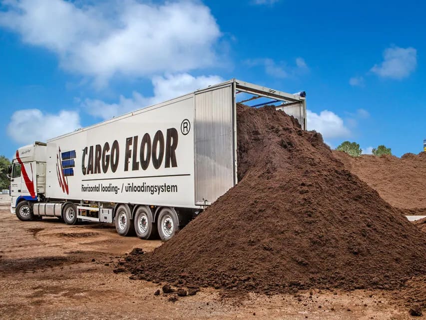 Poluprikolica Cargo Floor sa otvorenim zadnjim krajem, pored velike gomile zemlje istovarene pokretnim podom.