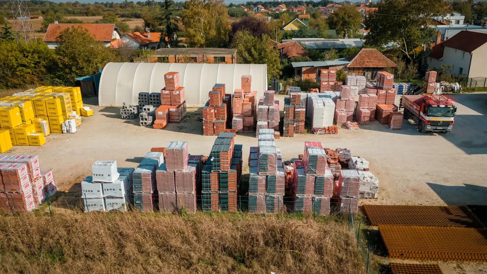 Palete Ytong blokova, opekarskih i betonskih blokova složene na otvorenom platou stovarišta Promax Trade, uz armaturne mreže i kamion za dostavu.