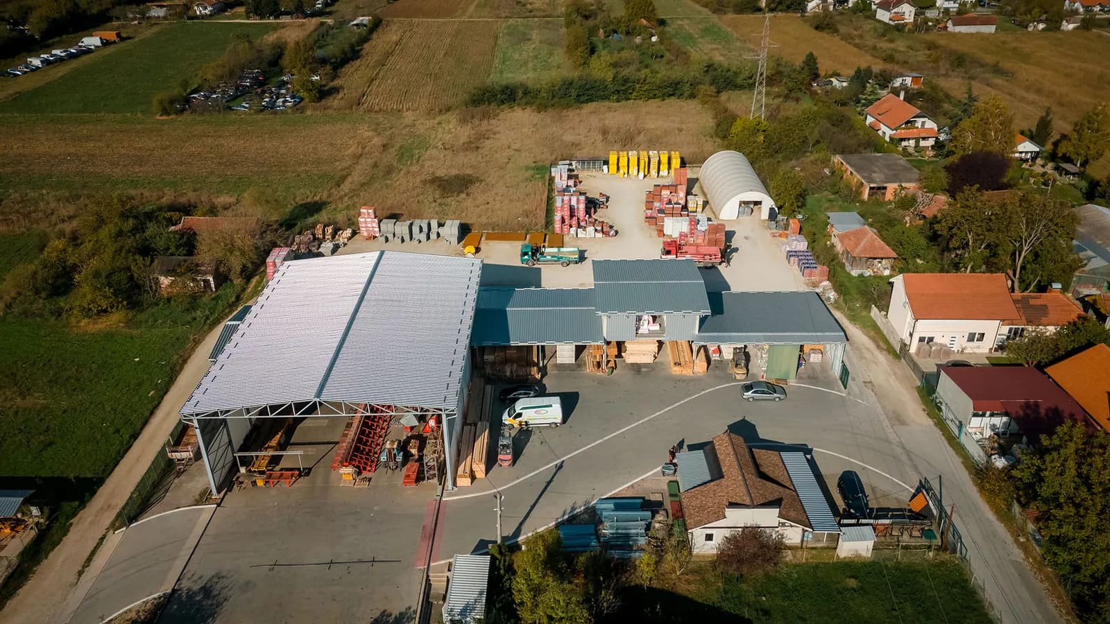 Pogled iz vazduha na stovarište Promax Trade: natkrivena hala, nadstrešnice sa građom i otvoreni plato sa paletama materijala.